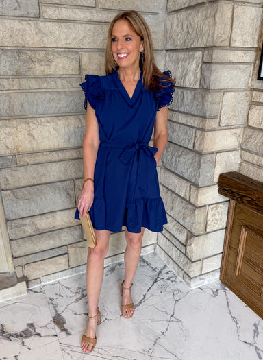 Navy blue dress with ruffle shoulders and flounce hem. Self tie waist belt and v neckline with scallop trim.