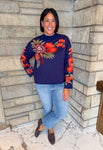 navy blue mock neck long sleeve sweater with bright flower print along arms and one side of chest